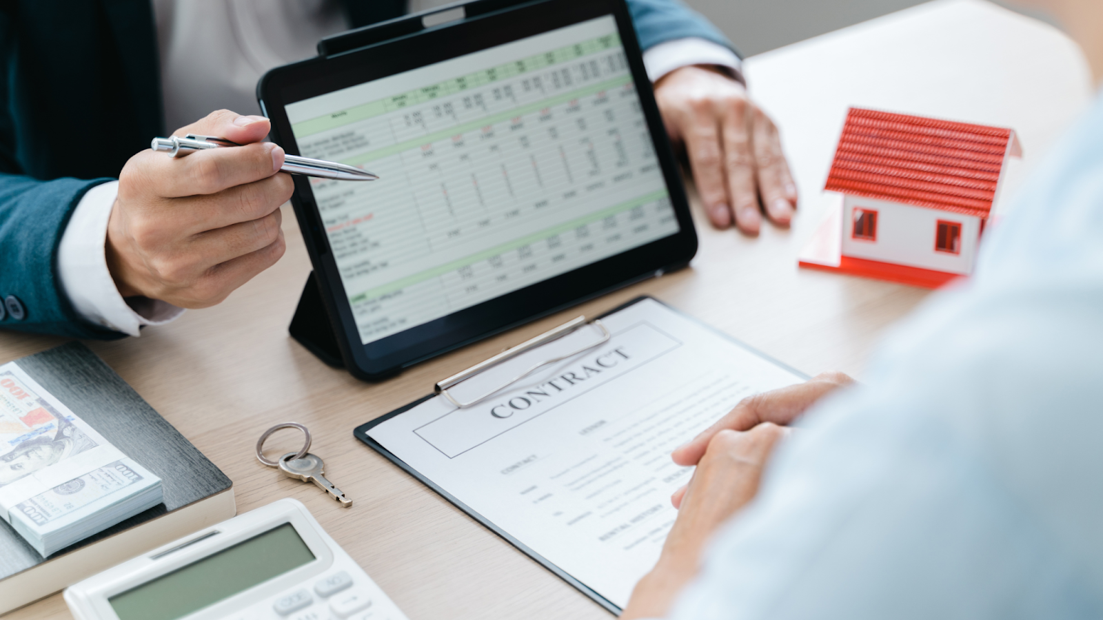  Real estate agent discussing contract details with a client, showing financial data from transaction coordinator on a tablet, with a house model, contract, and keys on the table.