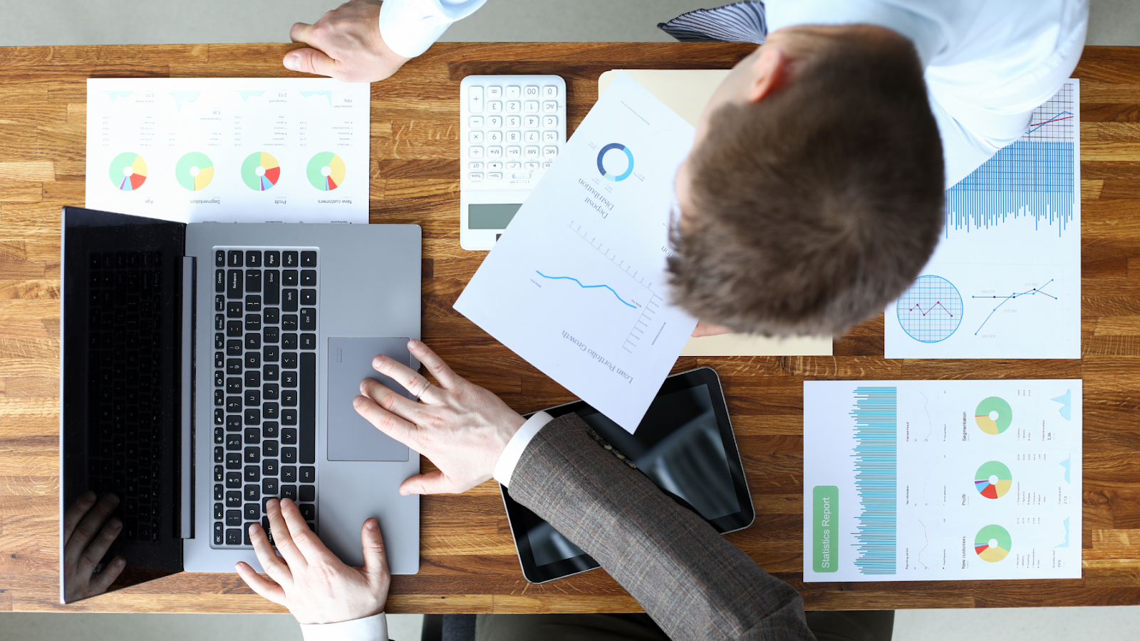 Two professionals working on a real estate transaction with charts, graphs, a laptop, and paperwork on a desk, representing streamlined workflows and transaction coordination.